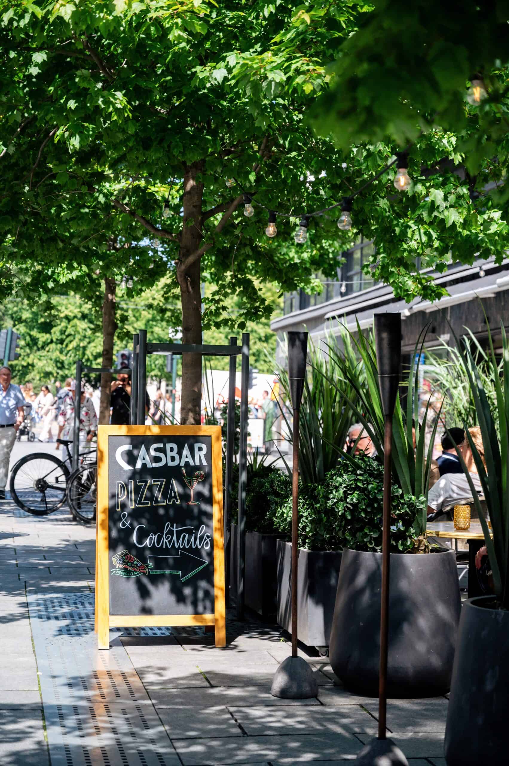 Uteservering ved Casbar i Oslo med grønne trær og uteservering. Perfekt for pizza, cocktails og sosi.