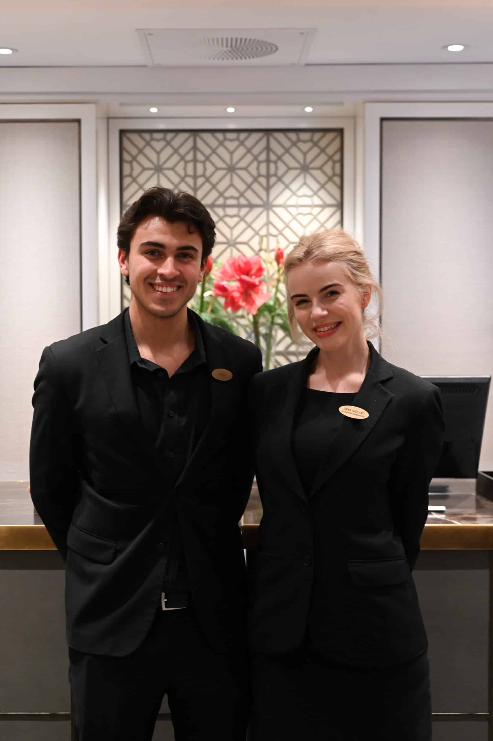 Two smiling hotel employees stand in front of the reception desk at Hotel Continental.